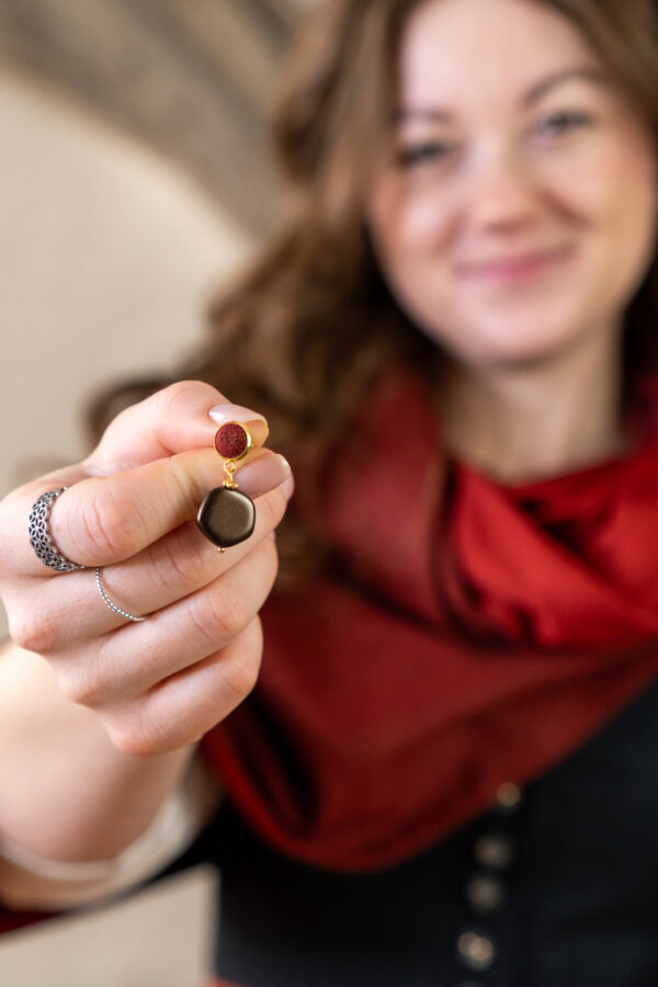 Rostroter Lodenohrring VERONIKA mit französischer Glasperle als Detailaufnahme in der Hand.