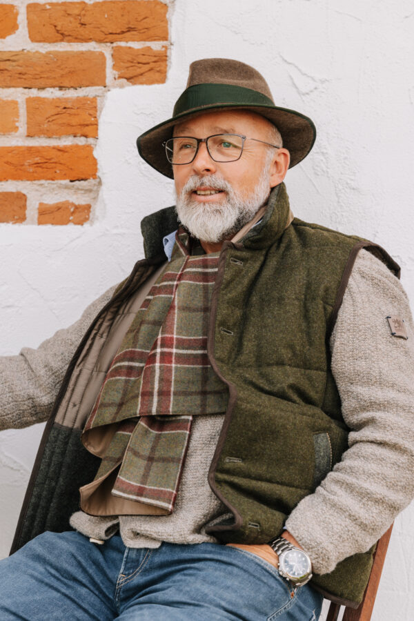 Mann trägt den karierten Lodenschal HANS zu einer grünen Lodenweste im Freien.